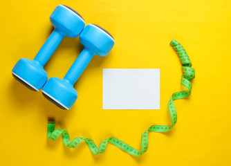 Sport weight loss concept. Dumbbells, ruler, pills on yellow background. Minimalism. White sheet of paper for copy space. Top view