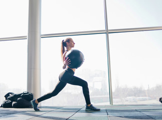 Fototapeta na wymiar Fitness young woman training with medicine ball in her hands against the background of a large panoramic window in the gym. Functional training