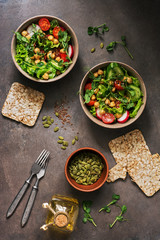 Bowls healthy vegetarian (vegan) salad,chickpea, lettuce, tomato, microgreen, radish, cucumber, flax seeds and pumpkin seeds with whole grain crispbreads on a dark brown background. Top view, flat lay
