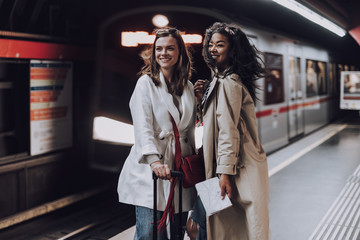 Two joyful young women standing on subway platform