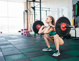Fototapeta na wymiar Young athlete woman in sportswear doing front squats with a barbell on the chest in the gym