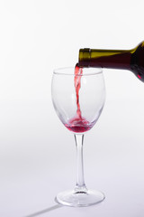 Pouring red wine into the glass on white background