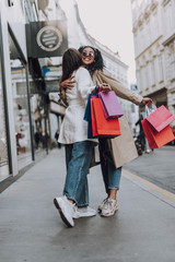 Happy afro american lady in trench coat hugging friend on the street