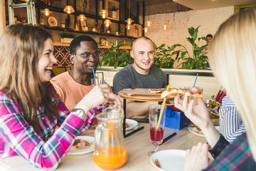 A company of multicultural  young people in a cafe eating pizza, drinking cocktails, having fun