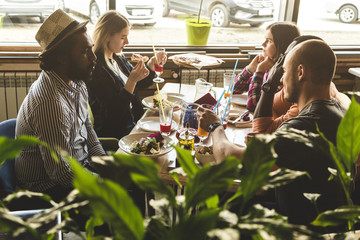 A company of multicultural  young people in a cafe eating pizza, drinking cocktails, having fun