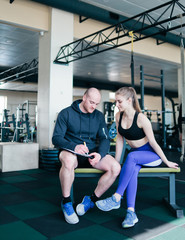 The concept of personal training. Instructor notes in notebook results  training sporty blonde woman sitting on a bench. Smiling sports couple