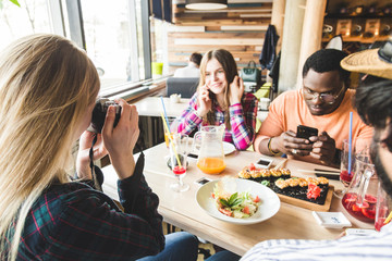 Group of young cheerful friends are sitting in a cafe, eating, drinking drinks. Friends take selfies and take pictures.
