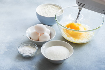 Mixer whipping eggs in a glass bowl and ingredients to create a cake 