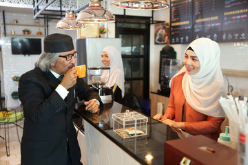 muslim customer businessman wearing black suit drinking coffee at counter with young muslim barista girls background