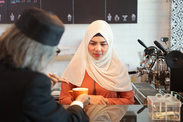 muslim customer businessman wearing black suit pointing to a cup of coffee and complain at counter with young muslim barista businesswoman