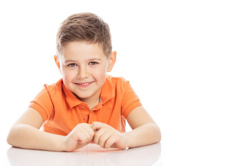 Cute boy sitting at the table and smiling. Close-up. Isolated on a white background.