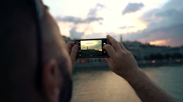 Young man taking photo of Budapest cityscape during sunset