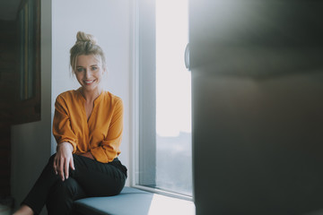 Cheerful lady sitting on the window sill and smiling