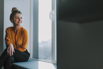 Woman looking away while sitting on the window sill