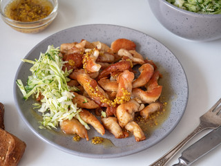 Fried chicken breast cut into small cubes with vegetable salad on a gray plate, shot at close range and cutlery on a white background with a salad of vegetables and toast from dark bread.
