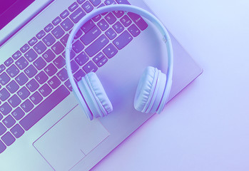 Modern laptop, wireless headphones. Gadgets. Duotone effect, holographic light. Top view, minimalism