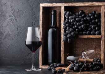 Luxury bottle of red wine with dark grapes inside vintage wooden box on black stone background....