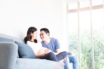Happy future Daddy with Pregnant Woman relaxing and smiling on Sofa Together with morning light from glass windows.