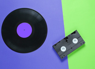 Outdated video cassette, retro audio cassette, vinyl record on a two-ton paper background, pop culture. Top view. Minimalism
