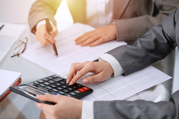 Two female accountants counting on calculator income for tax form completion hands close-up. Business and audit concept