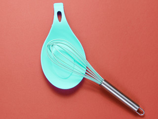 Silicone whisk for cooking with a metal handle on a stand on red background. Minimalism