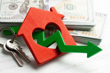 Arrow down and house with money on white wooden background. Falling market price of real estate.