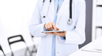 Female physician using digital tablet  while standing near reception desk at clinic or emergency hospital. Unknown doctor woman at work. Medicine concept