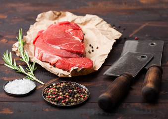 Fresh raw organic slice of braising steak fillet on paper with meat hatchets on dark wooden background. Salt and Pepper