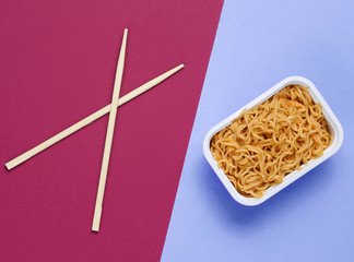 Instant noodles and chinese chopsticks on red purple background, minimalism. Top view