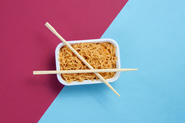 Instant noodles and chinese chopsticks on blue red background, minimalism. Top view