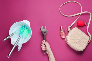 Women choose male work. Female hand holding a wrench on the background of bowl with kitchen tools, bags and bottle of perfume.