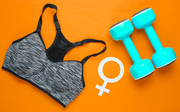 Female sport. Fitness concept. Sports bra, dumbbells, gender symbol feminism on orange background. Top view, minimalism