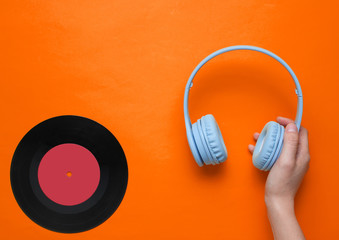 Women's hands hold over-ear headphones and vinyl record.on orange background. Pop culture, retro style, 80s. Minimalism. Top view. Flat lay