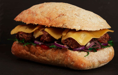 Closeup of delicious fresh homemade burger with lettuce, cheese, onions and tomatoes on dark background
