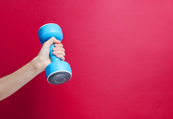 Female hand hold blue plastic dumbbells on red background. Copy space