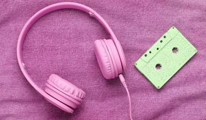 Pop culture attributes eighties. Headphones, audio cassette on pink denim background. Top view
