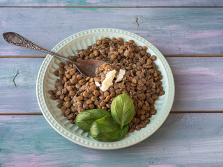 Boiled green lentils in a ceramic plate with a piece of butter on a turquoise tray