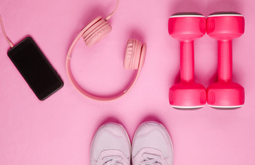 Obraz na płótnie Canvas Sport concept. Flat lay of smartphone with headphones, plastic dumbbells, sports sneakers on pink background. Top view