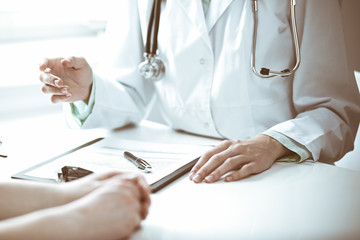 Doctor and  female patient sitting at the desk and talking  in clinic near window. Medicine and health care concept. Green is main color