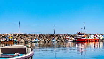 Colorful fishing boats in a harbour on a clear sunny day with blue skies reflected in the calm water.	