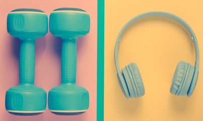 Plastic dumbbells, wireless headphones on color backgrounds. Fitness concept. Sport and music. Top view.