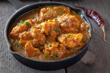 Close up traditional Indian butter chicken curry and lemon served with chapati bread in iron-cast. Wooden background.