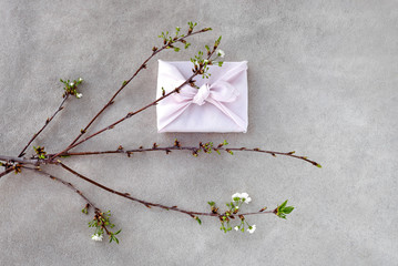 Japanese style gift box (Furoshiki) and blooming cherry branch on concrete background.
