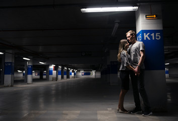 Obraz premium Loving young couple having fun and hugging in underground parking. Parking garage. Family have fun in the parking lot of the supermarket