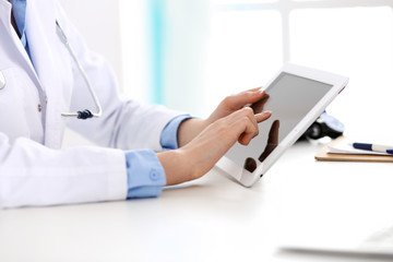 Doctor working table. Woman physician using tablet computer while sitting in hospital office close-up. Healthcare, insurance and medicine concept