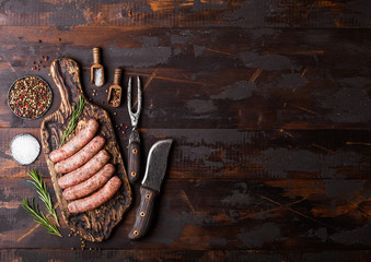 Raw beef and pork sausage on old chopping board with vintage knife and fork on dark wooden...