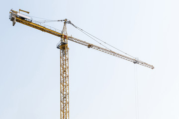 high-rise construction crane with a long arrow of yellow color against the blue sky over a new multi-storey building of concrete and brick under construction