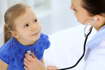 Doctor examining a little girl by stethoscope. Happy smiling child patient at usual medical inspection. Medicine and healthcare concepts