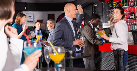 Cheerful male and female colleagues having fun on corporate party in bar