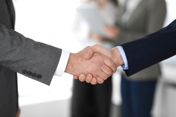 Business people shaking hands at meeting or negotiation, close-up. Group of unknown businessmen and women in modern office at background. Teamwork, partnership and handshake concept